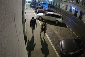 Na zdjęciu widoczni są dwaj mężczyźni idący nocą po chodniku