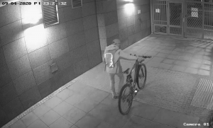 Na zdjęciu widoczny jest mężczyzna prowadzący nocą po chodniku skradziony rower