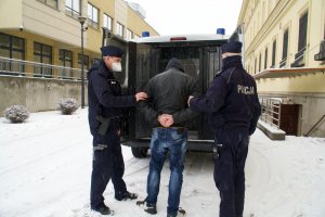 Na zdjęciu widoczny jest zatrzymany mężczyzna stojący z policjantami