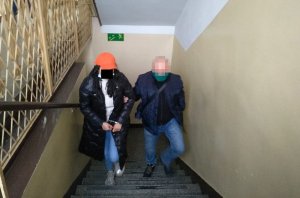 Na zdjęciu widoczna jest kobieta prowadzona po schodach przez nieumundurowanego policjanta