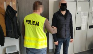 Na zdjęciu widoczny jest zatrzymany mężczyzna, który stoi w pokoju przy nieumundurowanym policjancie