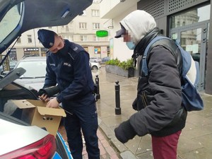 Na zdjęciu widoczny jest policjant rozdający odzież zimową bezdomnym