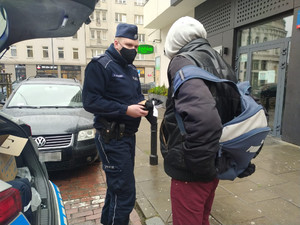 Na zdjęciu widoczny jest policjant rozdający odzież zimową bezdomnym