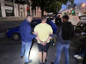 Na zdjęciu widoczny jest zatrzymany mężczyzna w asyście policjantów